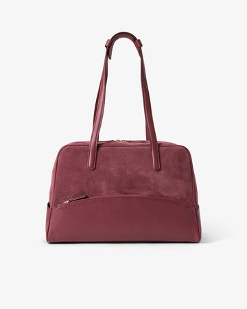 A burgundy leather duffel bag with dual top handles and a front zippered pocket, shown against a plain white background.