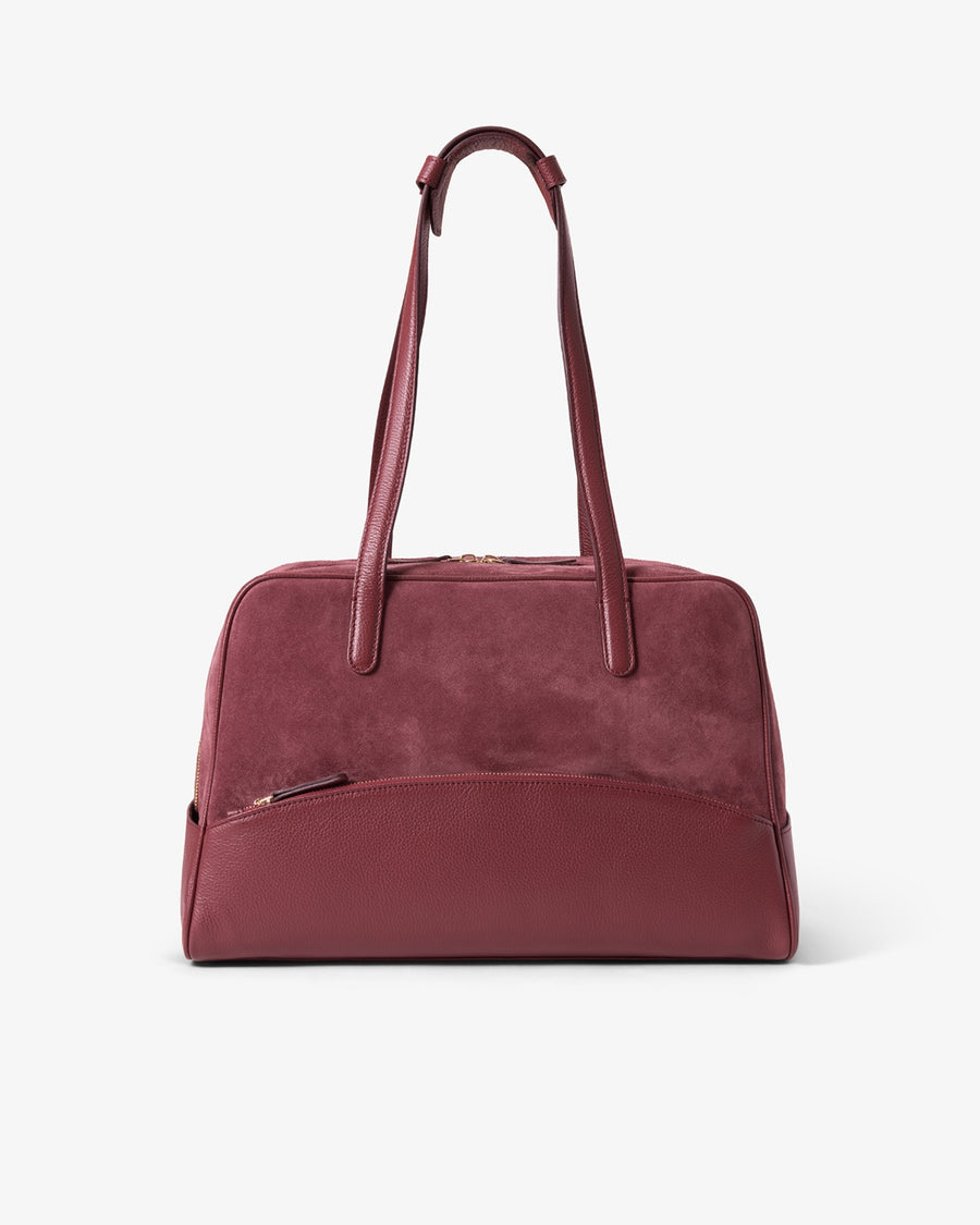 A burgundy leather duffel bag with dual top handles and a front zippered pocket, shown against a plain white background.