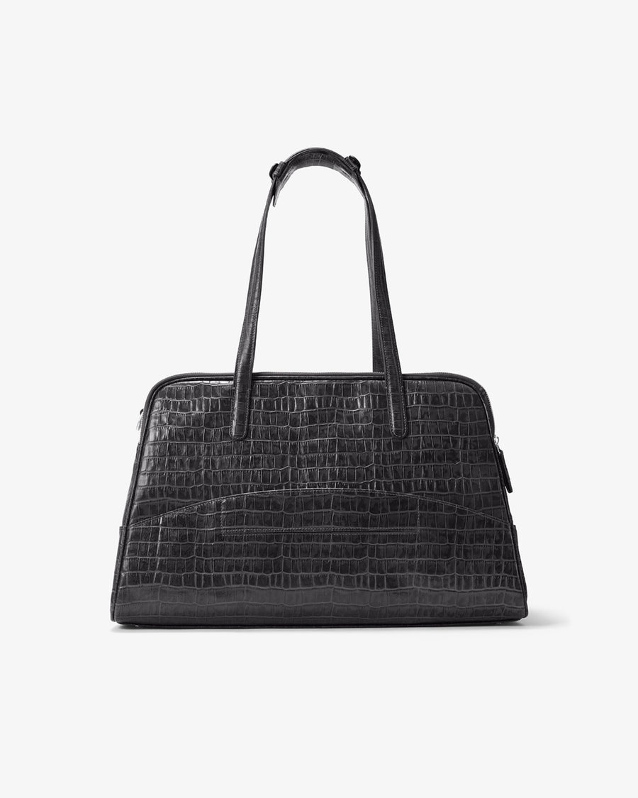 A black crocodile-embossed leather handbag with dual top handles and a luggage strap, shown against a plain light gray background.