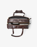 A dark brown crocodile-embossed zippered leather bag shown open from a top-down view, revealing its interior and contents, on a clean white background.