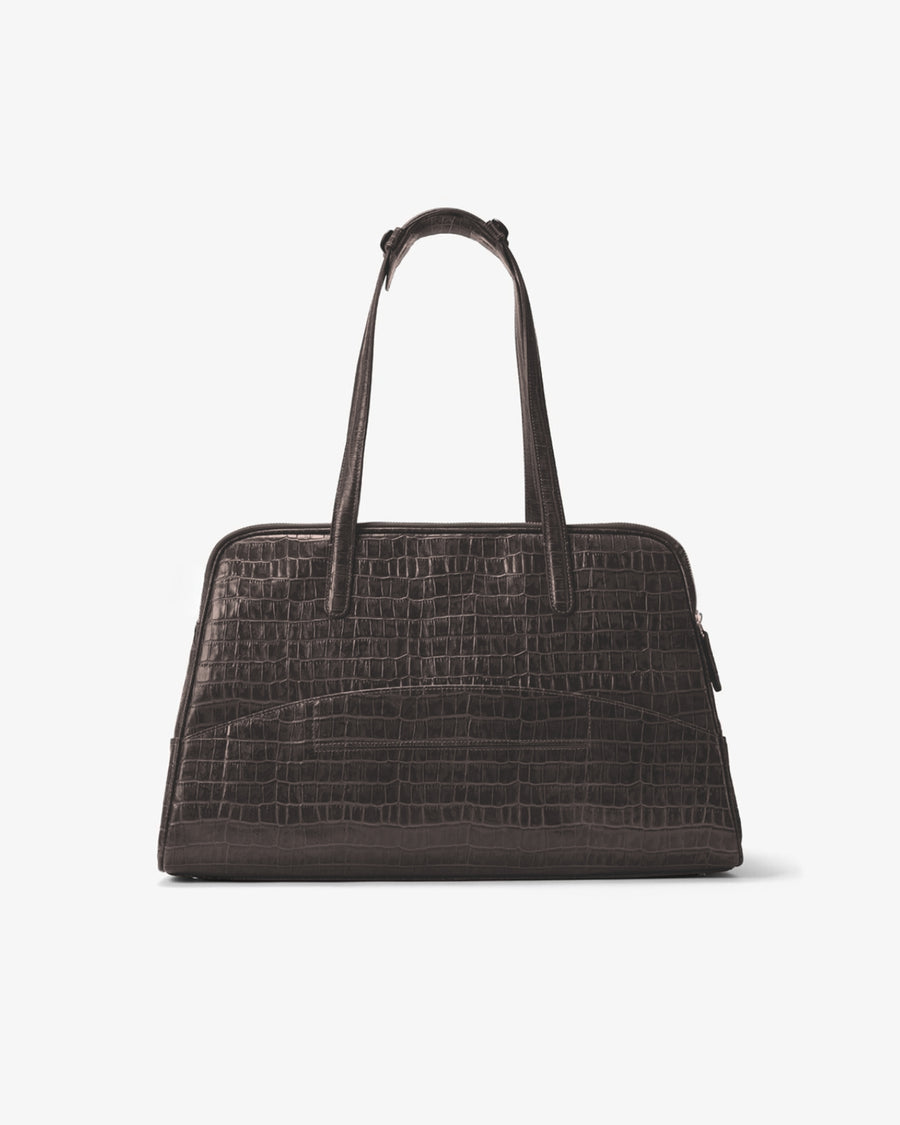 A dark brown crocodile-embossed leather handbag with dual top handles, and a luggage strap, shown from the back against a plain light gray background.