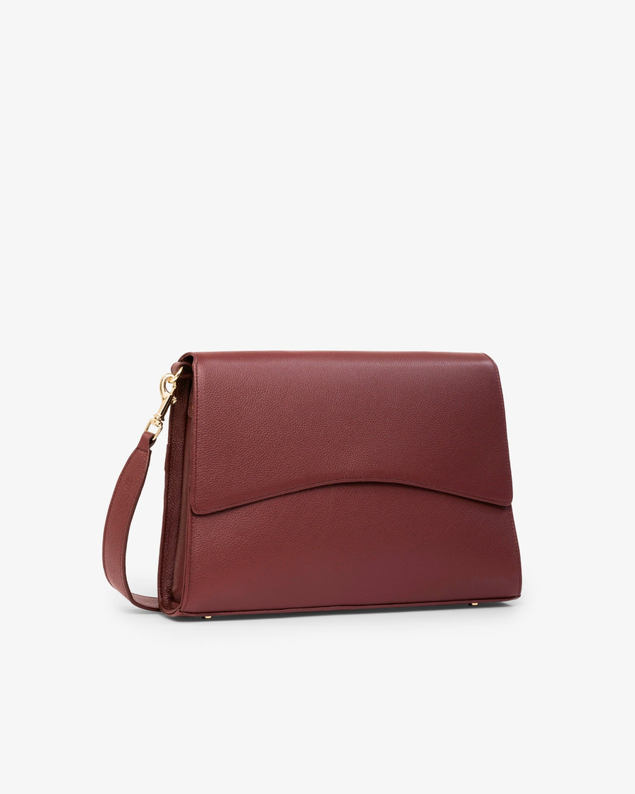 A burgundy leather clutch bag with a curved front flap and a matching shoulder strap, featuring gold-tone hardware, shown against a plain white background.