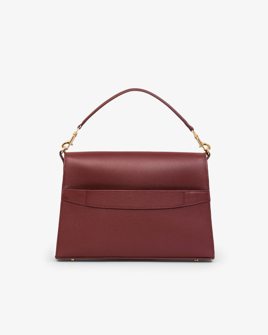 A structured burgundy leather handbag with a top handle, gold-tone hardware, and a luggage strap, shown against a plain light gray background.