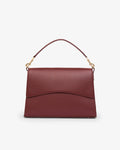 A structured burgundy leather handbag with a top handle, gold-tone hardware, and a curved flap closure, shown against a plain white background.