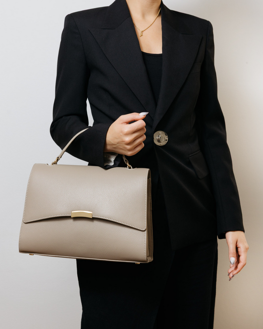 Person wearing a black suit holding a beige handbag against a neutral background