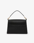 A structured black leather handbag with a top handle, gold-tone hardware, and a luggage strap shown against a plain light gray background.