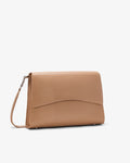 A tan leather bag with a curved flap and a matching strap, shown from a three-quarter angle on a light gray background.