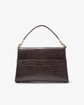 A dark brown crocodile-embossed leather handbag with a single top handle and gold-tone hardware, featuring a luggage strap, shown against a plain white background.