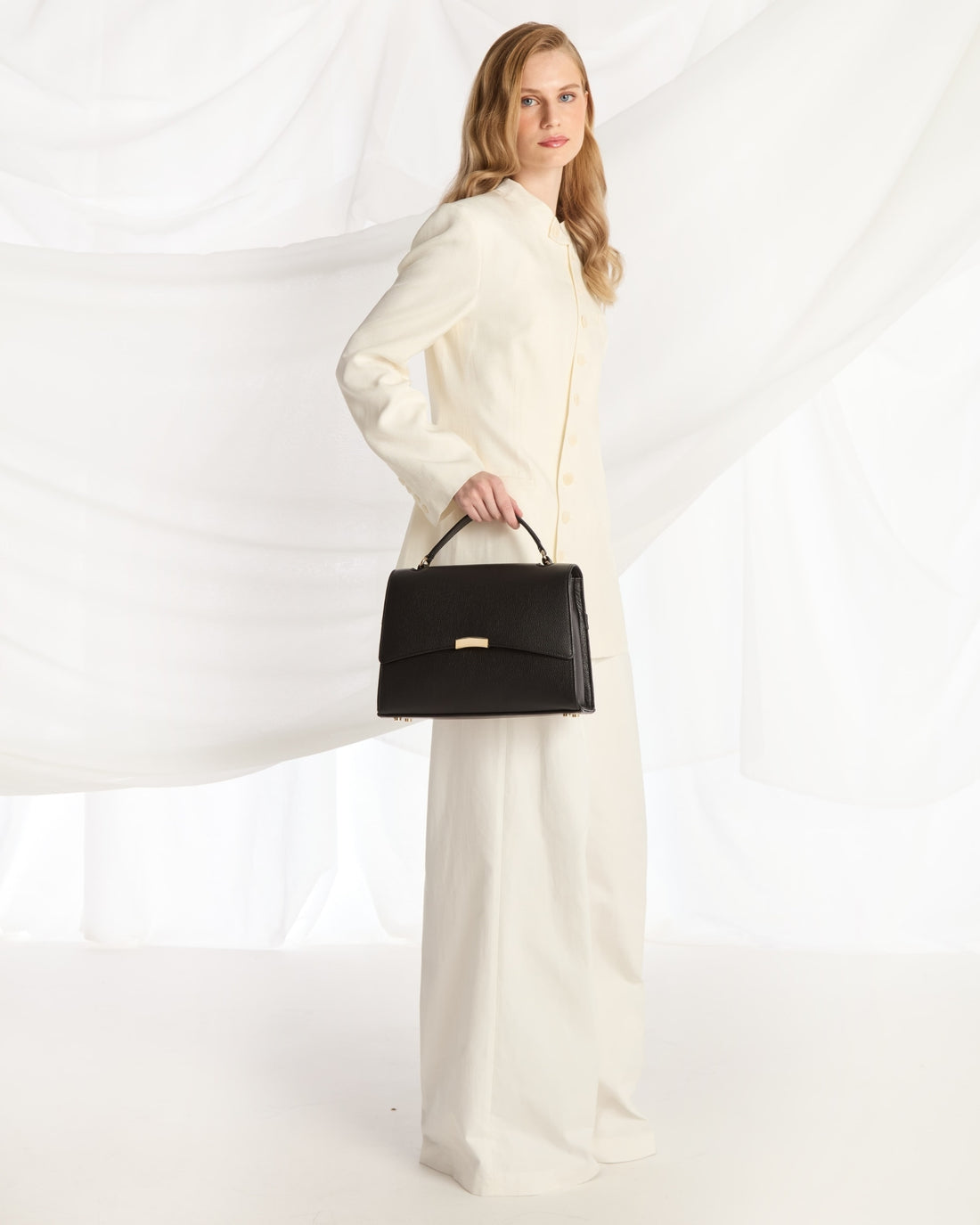 A structured black leather handbag with a top handle and a small gold-tone metal accent on the front, photographed against a clean white background.