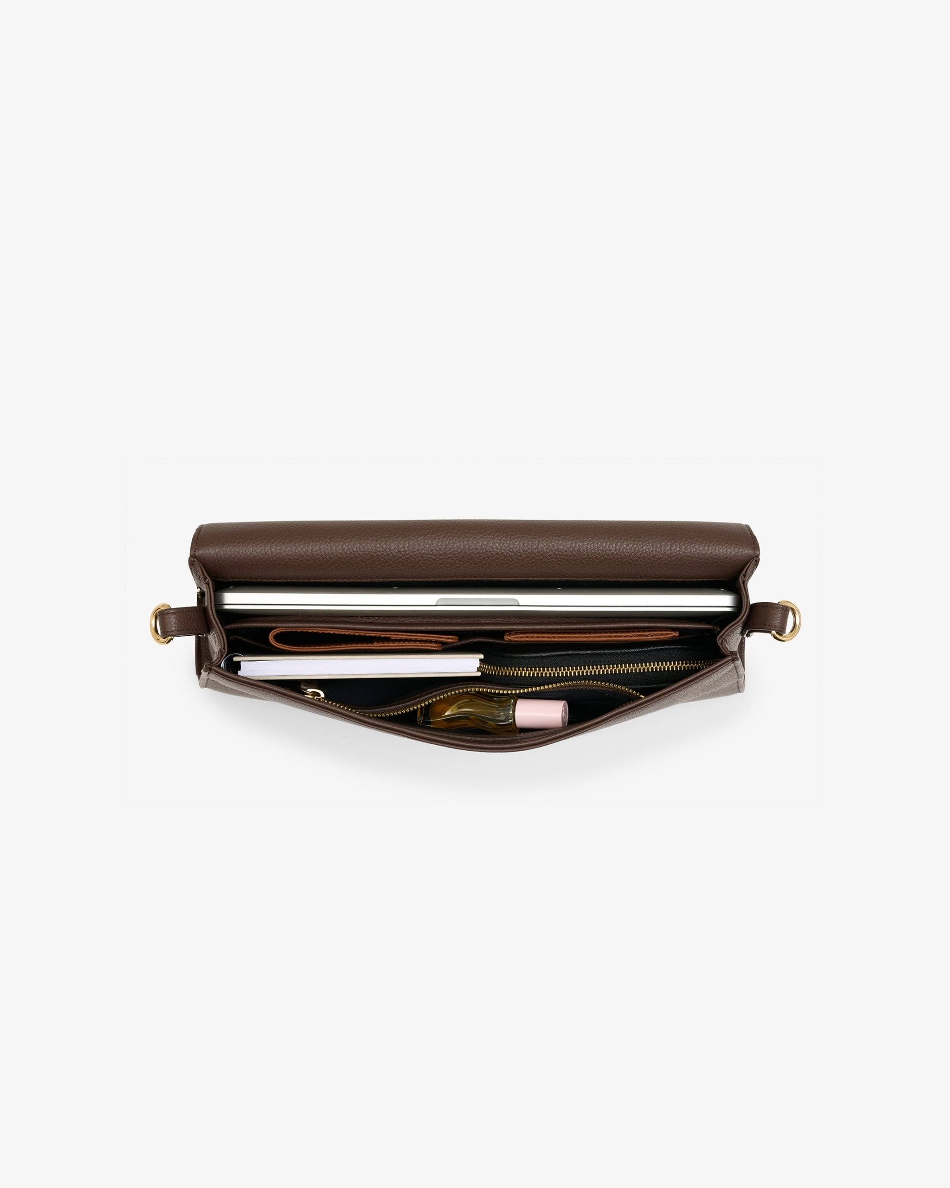 A brown leather  bag shown open from a top-down view, revealing its interior compartments filled with travel accessories like a a passport holder, a pen, and a small pouch, set against a plain light gray background.