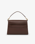 A structured dark brown leather handbag with a top handle, gold-tone hardware, and a luggage strap, shown against a plain light gray background.