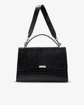 A black crocodile-embossed leather handbag with a top handle and shoulder strap, featuring a small silver metal accent on the front, set against a plain light gray background.
