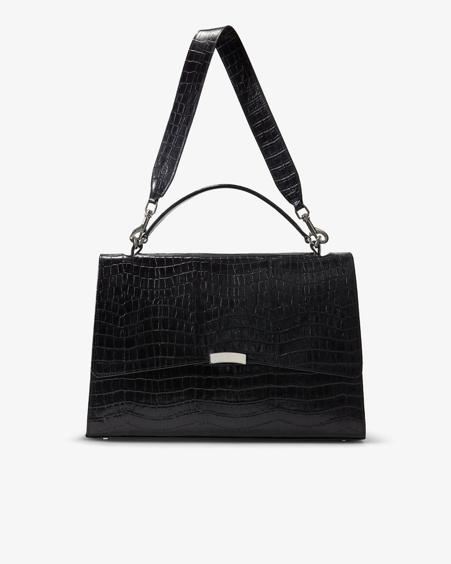 A black crocodile-embossed leather handbag with a top handle and shoulder strap, featuring a small silver metal accent on the front, set against a plain light gray background.