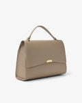 A structured taupe leather handbag with a top handle and a small gold-tone metal accent on the front flap, shown against a plain white background.