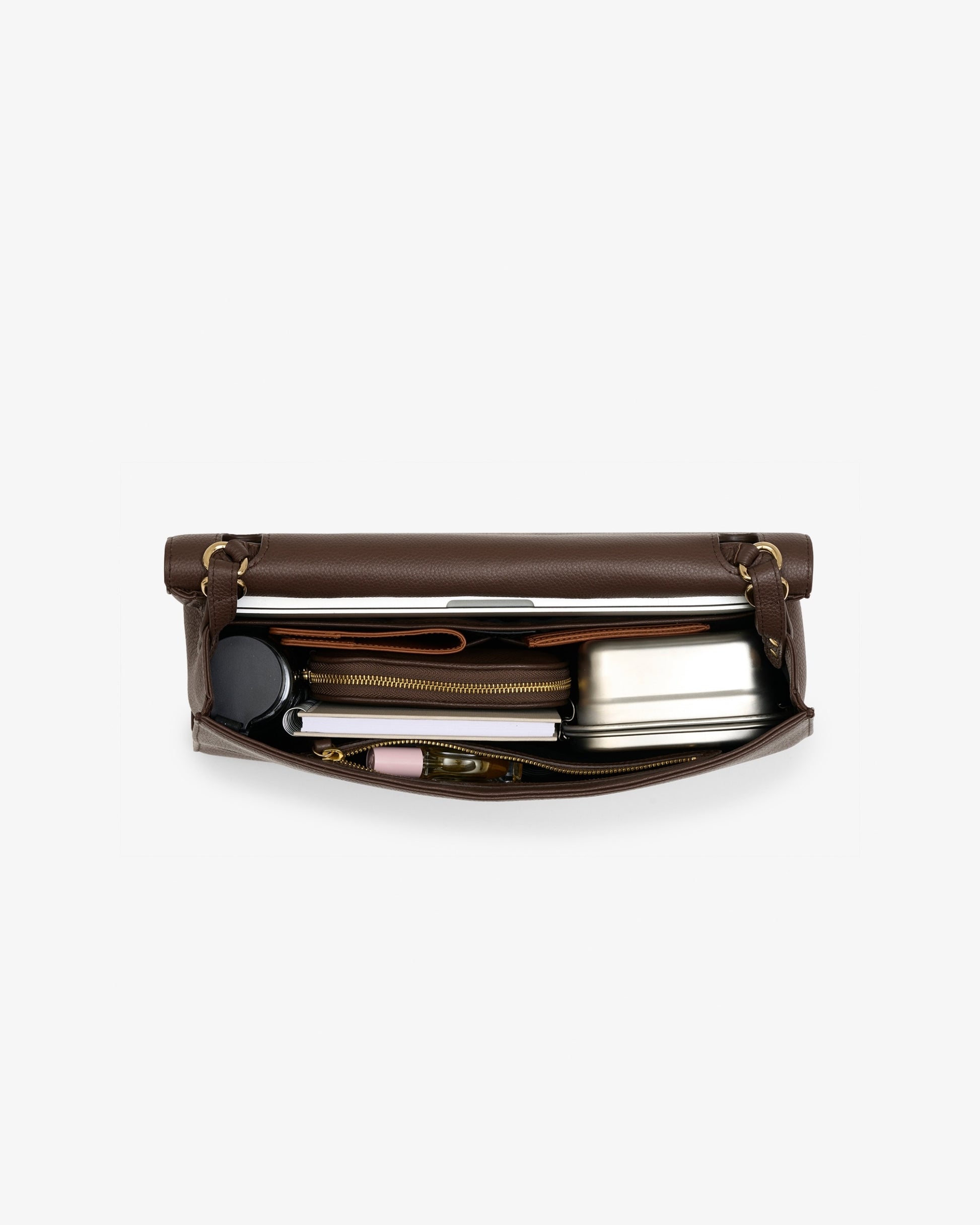 An open brown leather bag shown from above on a light gray background. Inside, a silver metal travel mug, a black circular item, and other small accessories are neatly arranged.