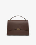 A dark brown textured leather handbag with a top handle and a gold-tone metal accent on the front flap, shown against a plain white background.
