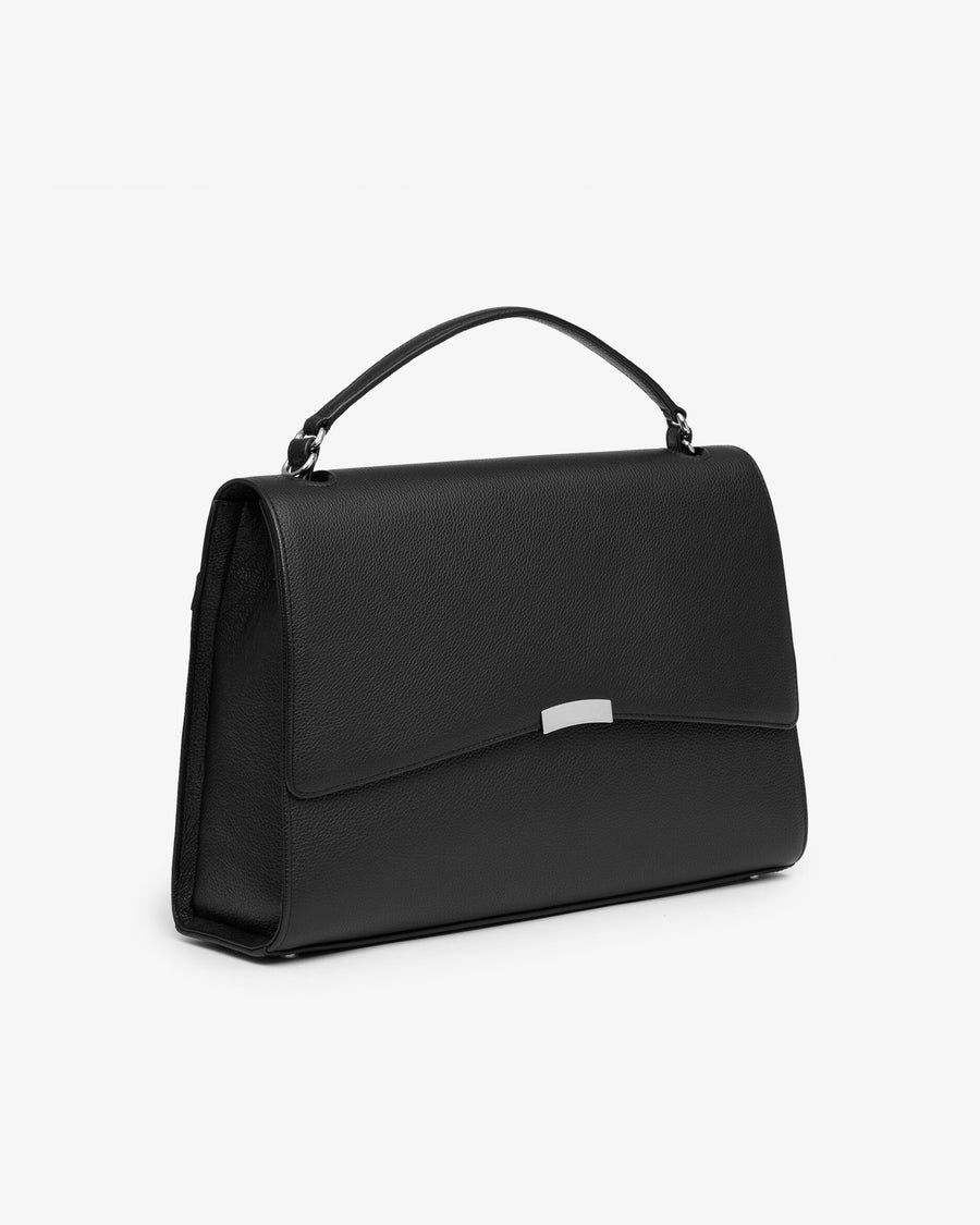 A black leather top-handle handbag with a gold-tone metal accent on the front flap, shown from a three-quarters angle against a plain white background.
