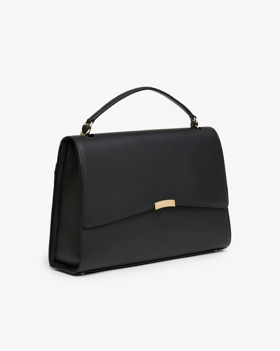 A black leather top-handle handbag with a gold-tone metal accent on the front flap, shown from a three-quarters angle against a plain white background.