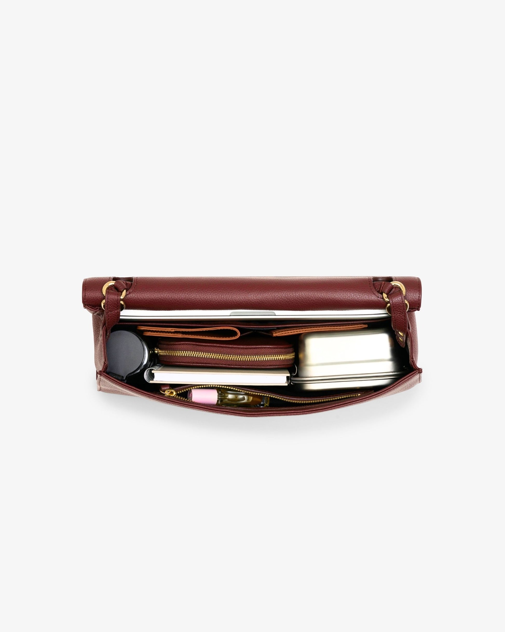 A burgundy leather zippered briefcase shown open from a top-down view, revealing a silver metal lunchbox, a black circular item, and other small accessories inside, set against a plain white background.