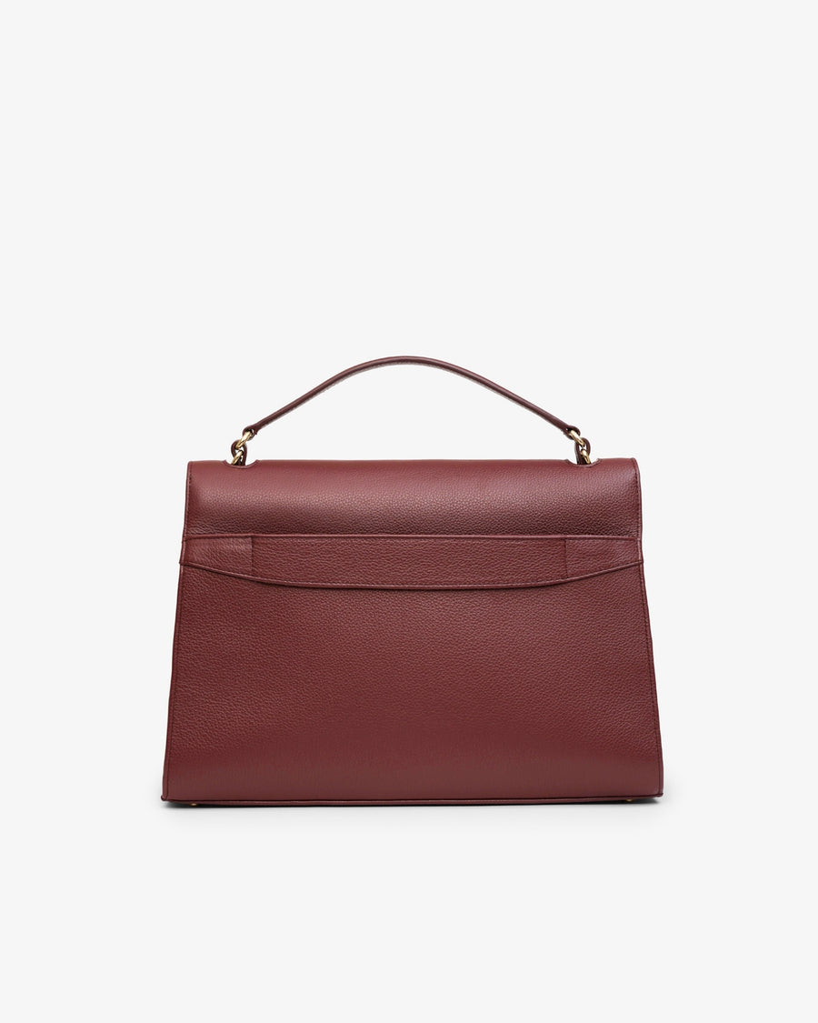 A structured burgundy leather handbag with a top handle and gold-tone hardware, featuring a luggage strap, photographed against a clean white background.