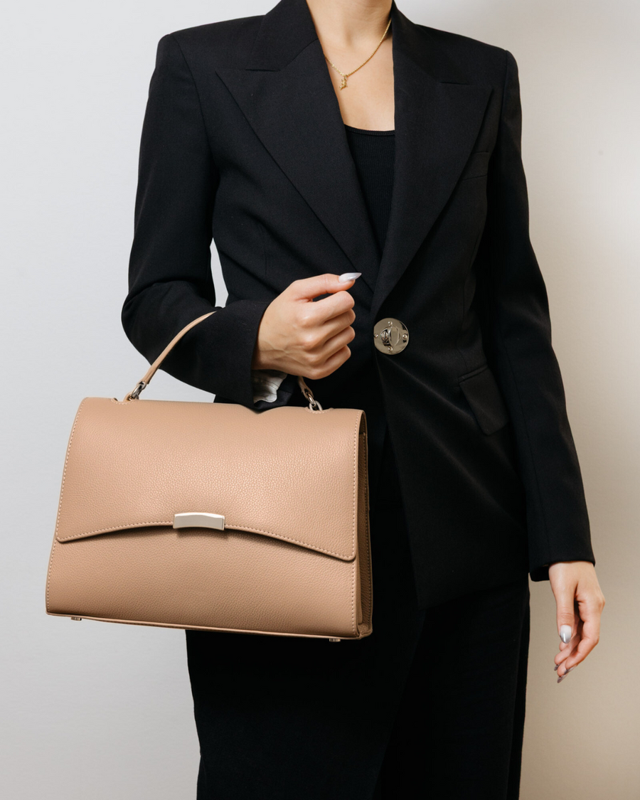 Person wearing a black suit holding a beige handbag against a neutral background