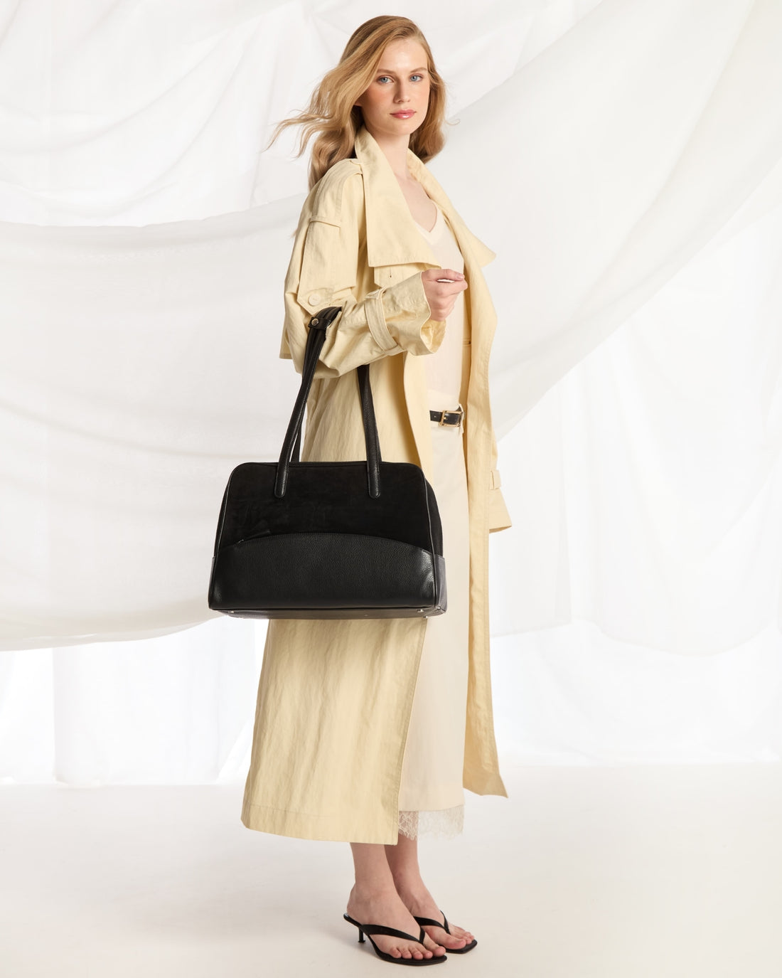A black shoulder bag with a smooth leather base, a black suede upper section, and dual top handles, shown against a plain light gray background.