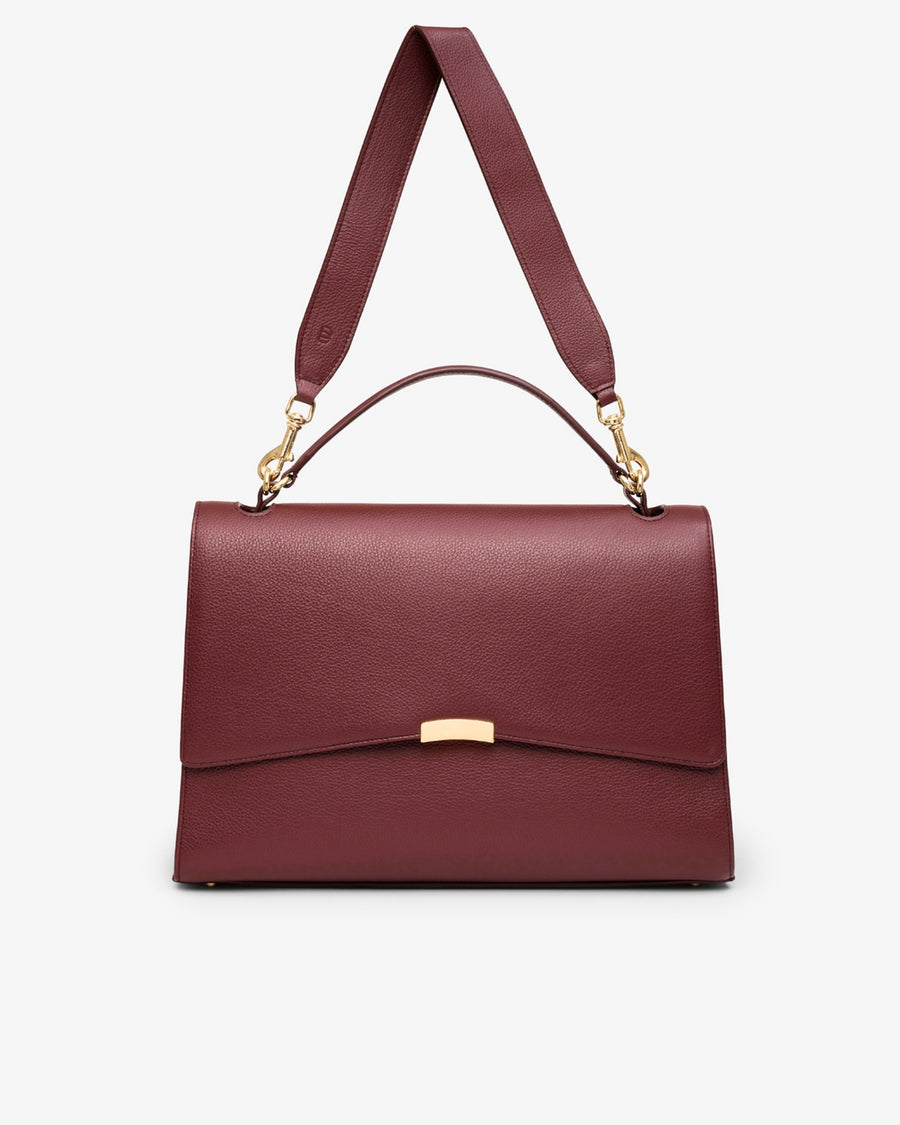 A structured burgundy leather handbag with a top handle, an adjustable shoulder strap, and gold-tone hardware, shown against a plain light gray background.