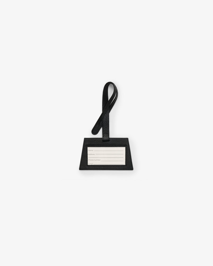 A minimalist black luggage tag with a loop handle and a white rectangular nameplate, centered on a light gray background.