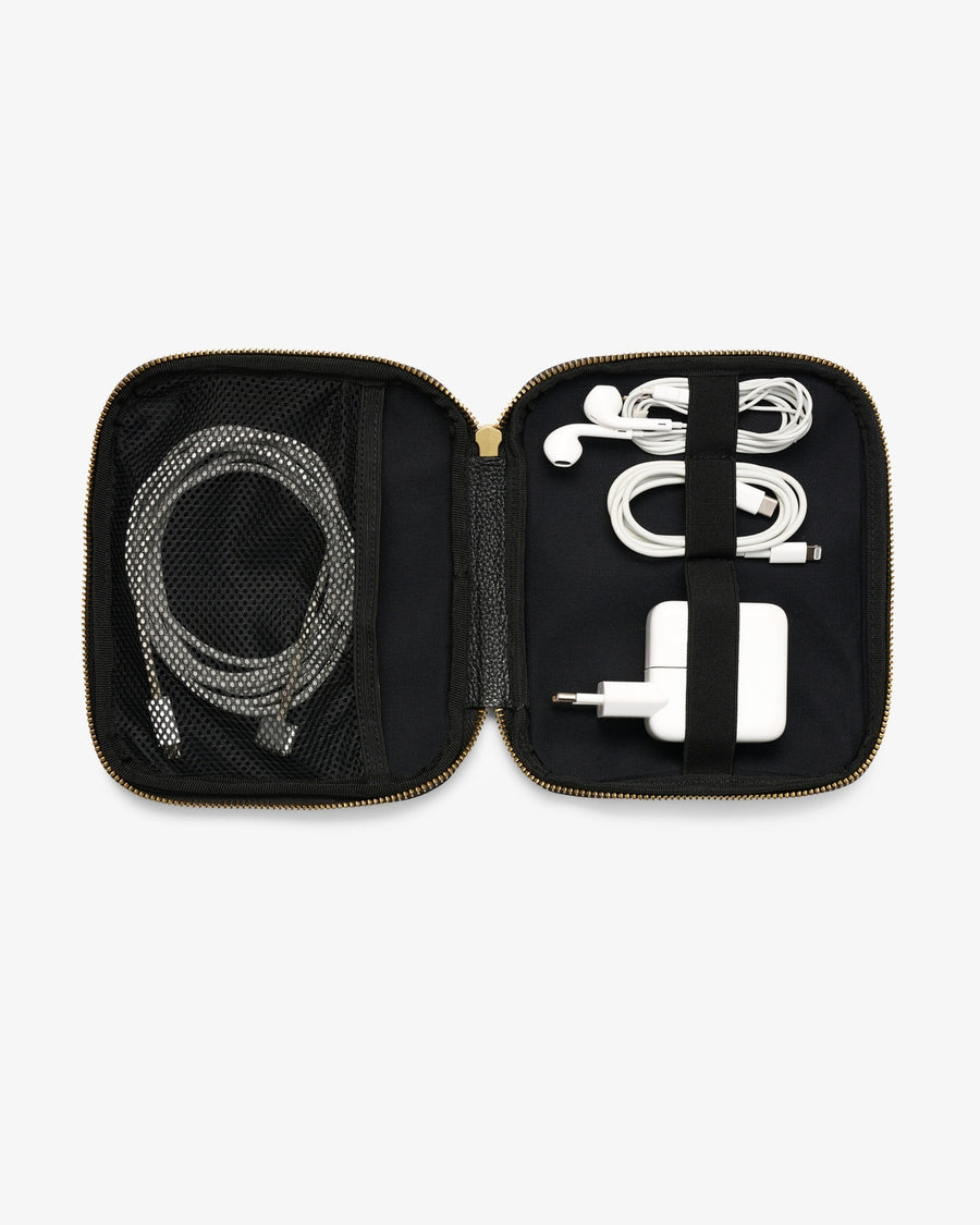 An open black zippered accessory organizer case with gold-tone zippers, shown on a light gray background. Inside, a gray braided charging cable is stored in a mesh pocket on the left, and a white earbud cable with a white charging adapter is secured by a black elastic band on the right.