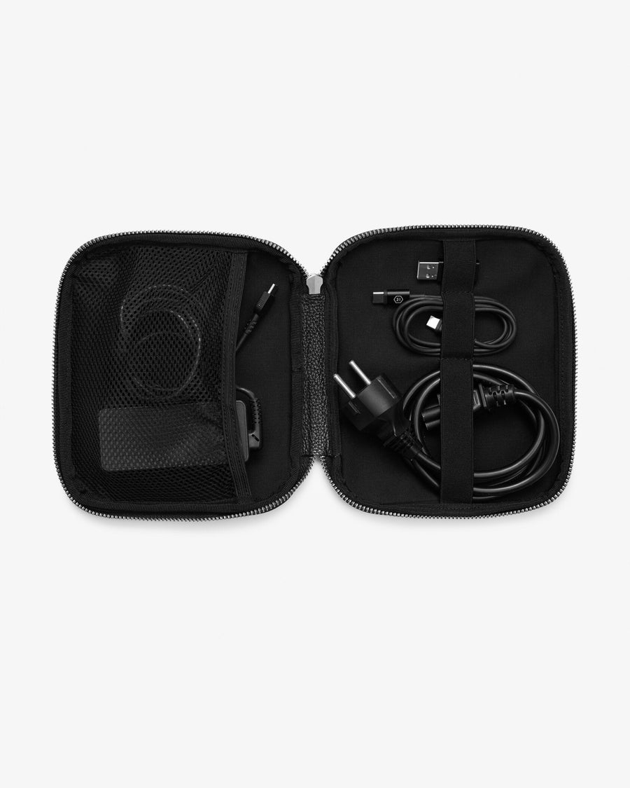 An open black zippered carrying case shown from above, containing black cables, a USB-C connector, and a small black accessory in mesh and elastic compartments, on a light gray background.