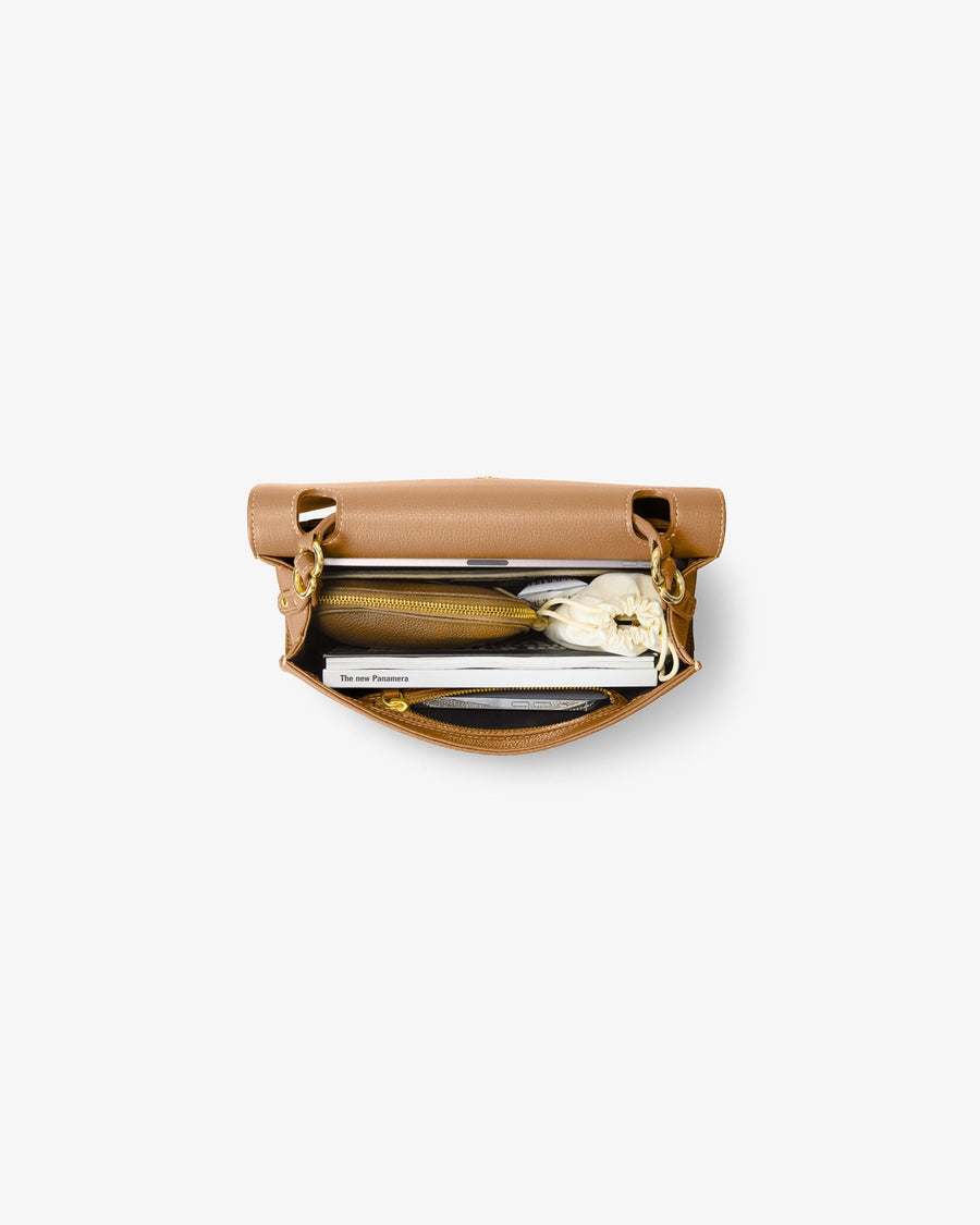 A top-down view of a tan leather briefcase bag with gold-tone hardware, shown open with a laptop and accessories inside, set against a plain light gray background.