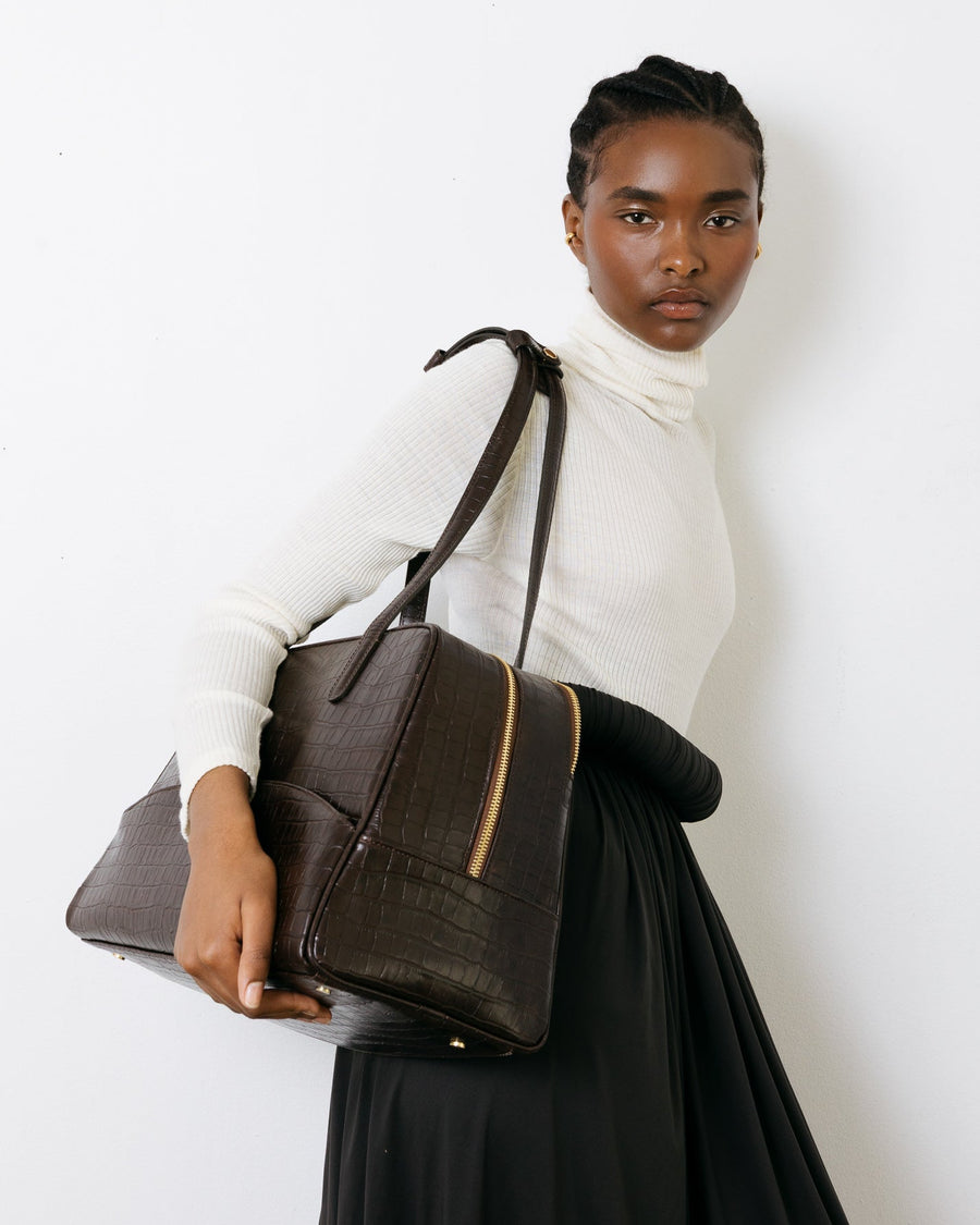 Woman holding a brown leather bag against a white background