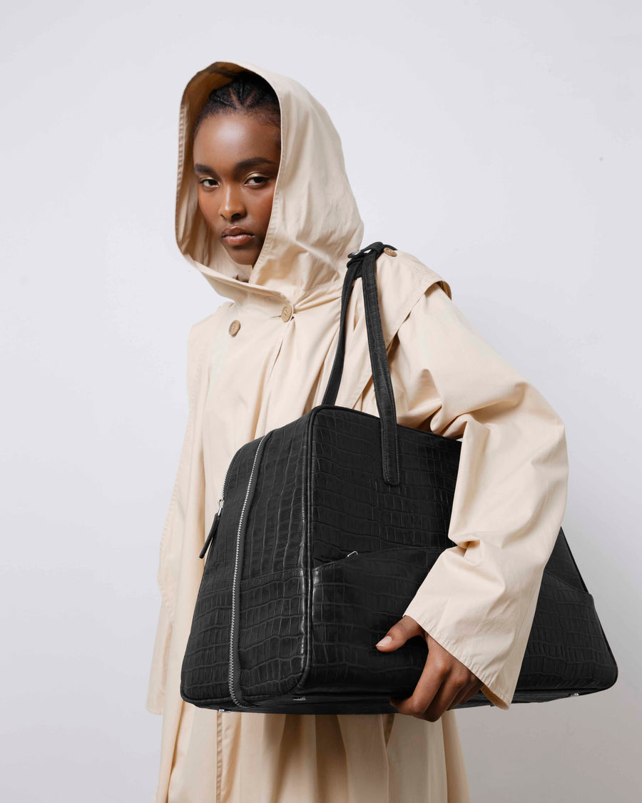 Person wearing a beige raincoat holding a black bag against a white background