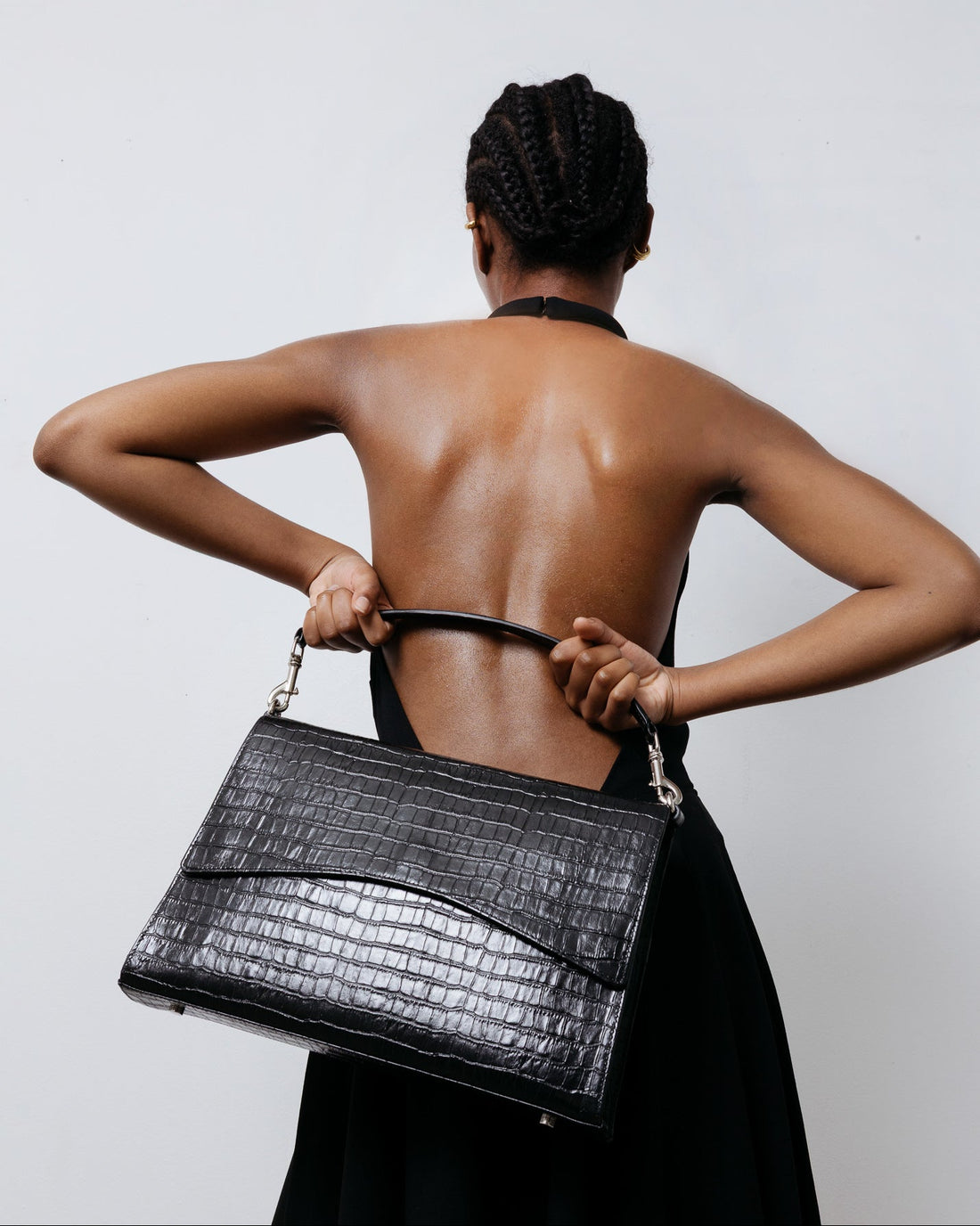 Woman holding a black handbag against a plain background