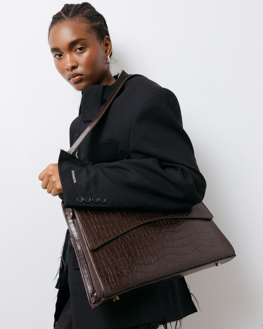 Person holding a brown leather bag against a white background
