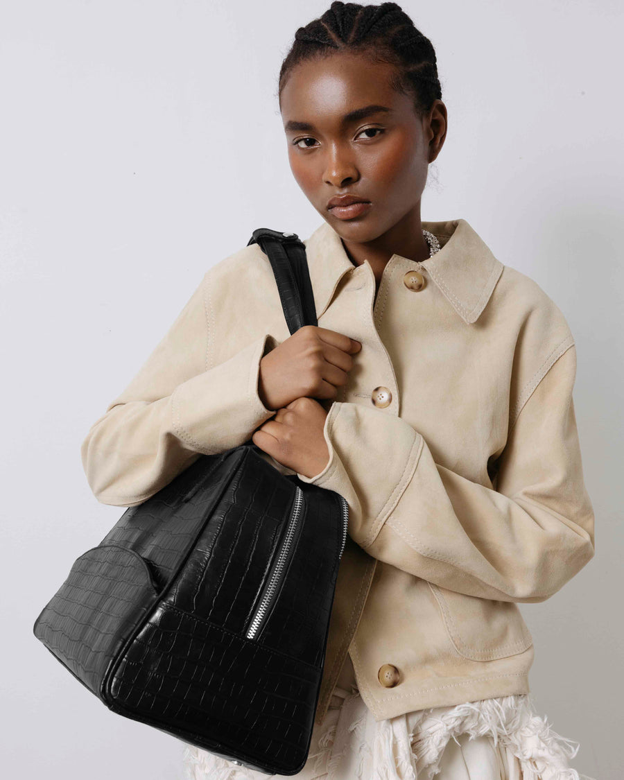 Woman holding a black handbag against a plain background