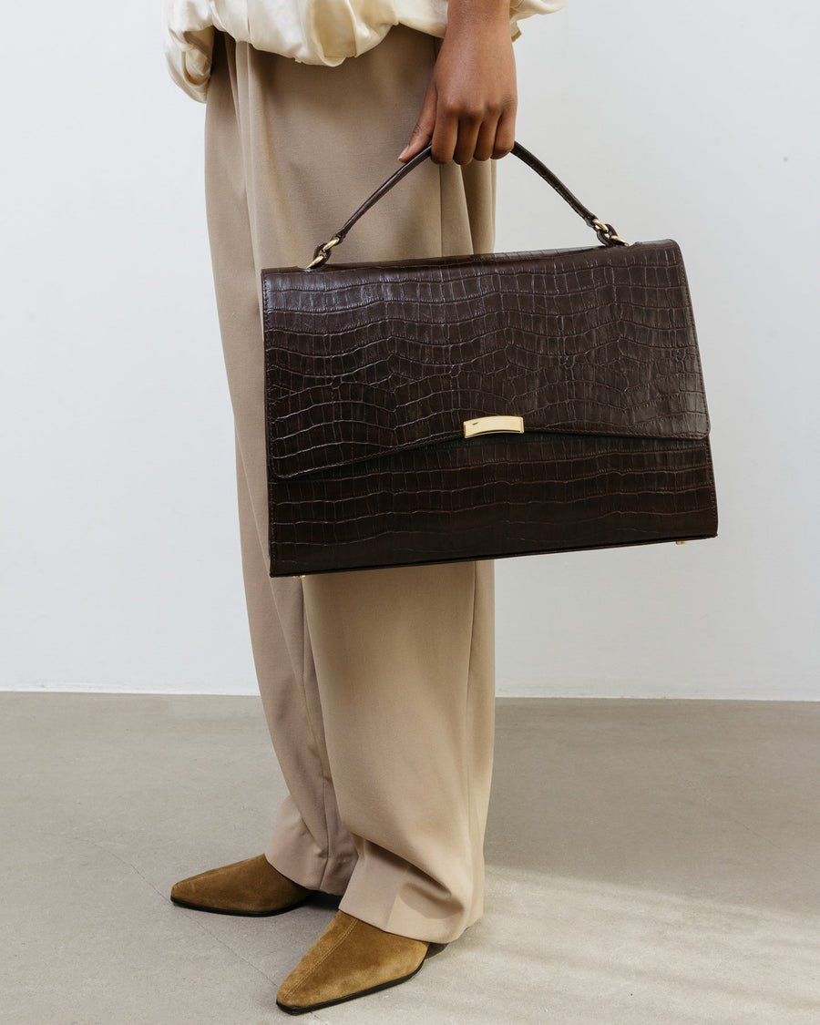 Person holding a dark brown textured handbag against a plain background