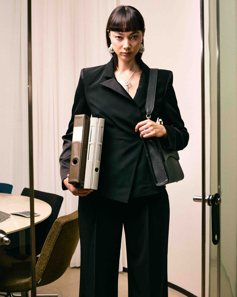 A woman in an office setting, carrying a black leather shoulder bag. 
