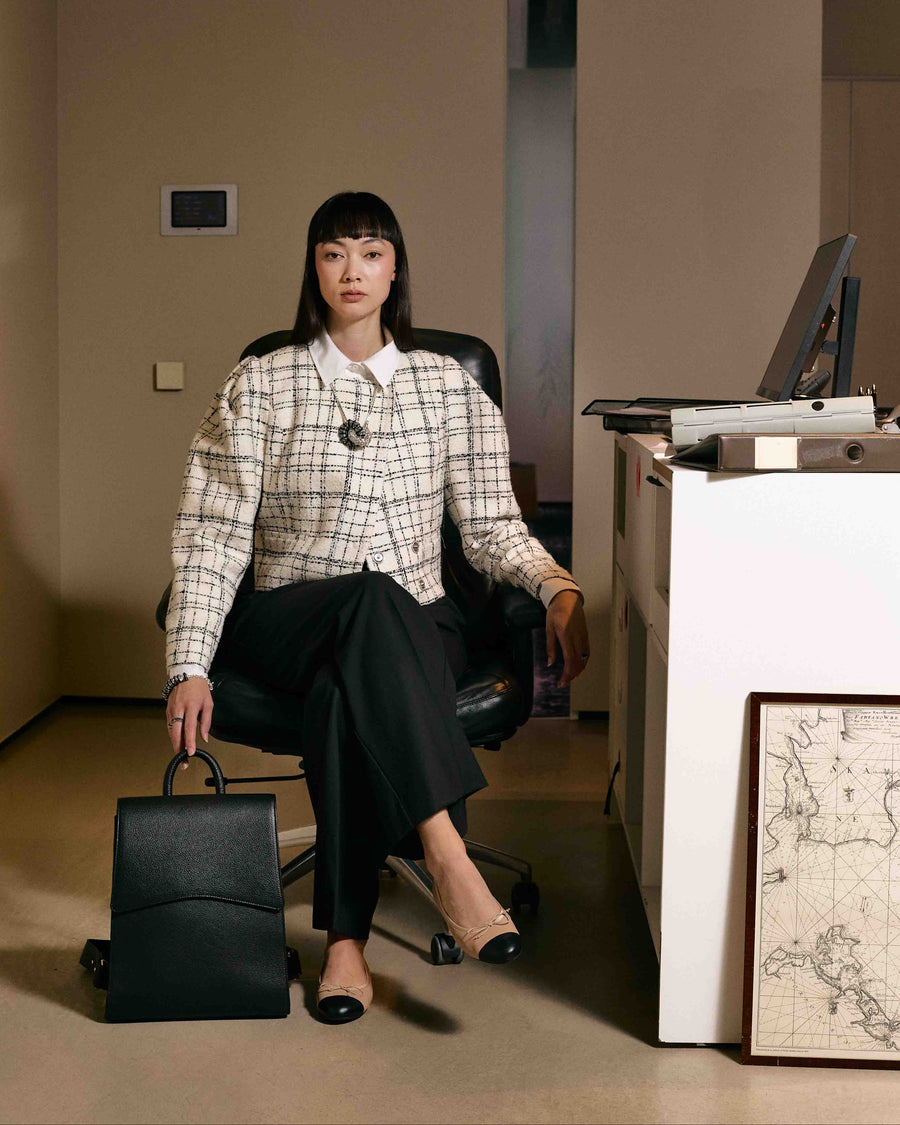 A woman sitting down in an office, holding a black leather backpack with a top handle.