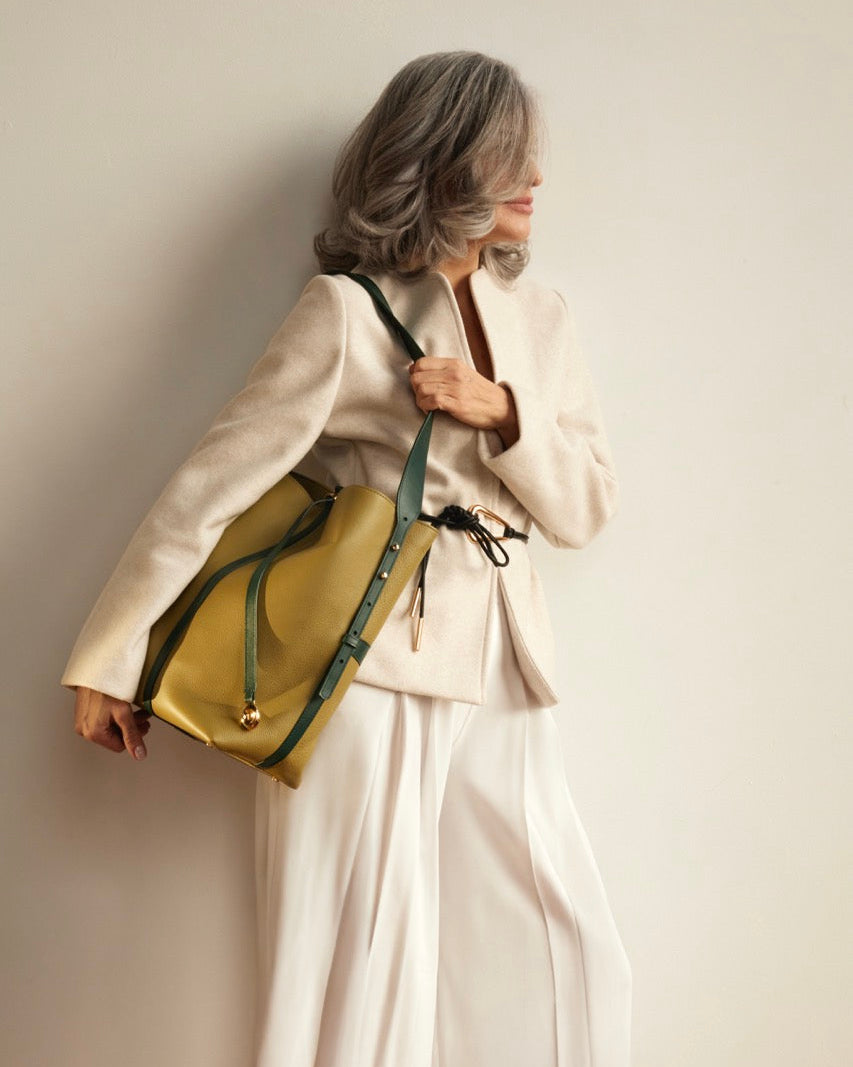 An olive green leather bucket bag with a dark green vertical strap detail and a gold-tone medallion, shown on a clean white background.