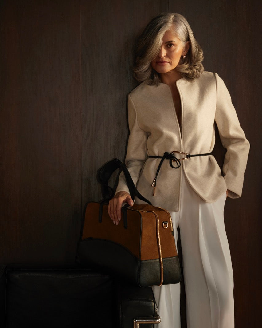 Woman in a white outfit holding a brown leather bag against a dark background
