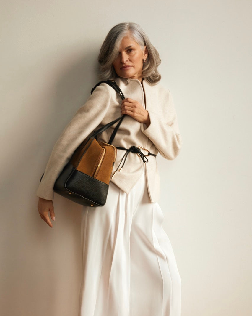 Woman holding a black and brown handbag against a plain background. 