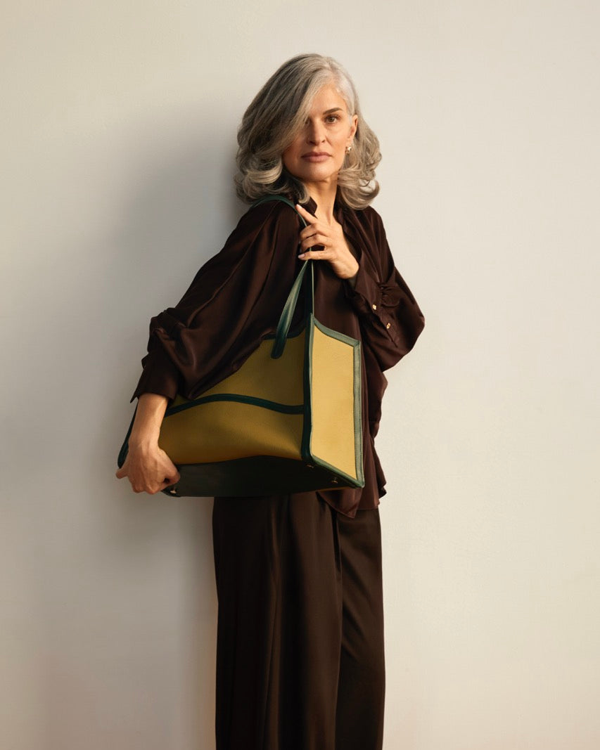 A structured leather tote bag with a light olive green body and dark forest green trim and handles, shown against a plain light gray background.