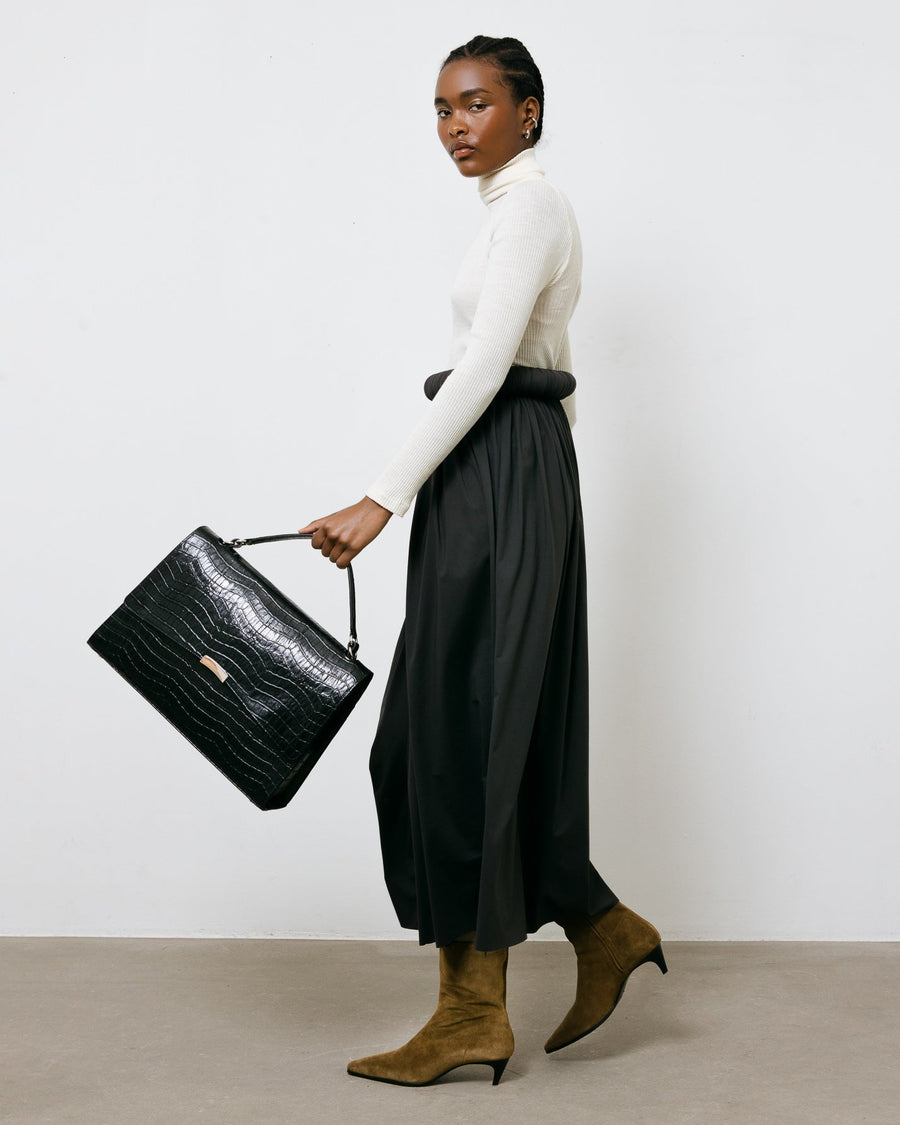 Woman holding a black handbag against a white background