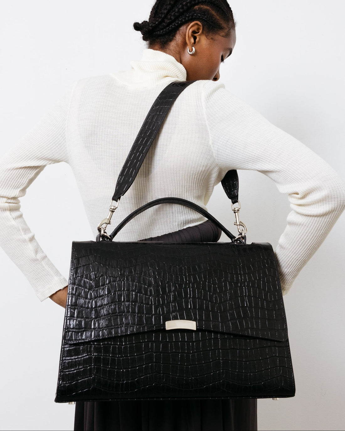 Person wearing a black textured handbag on a plain background