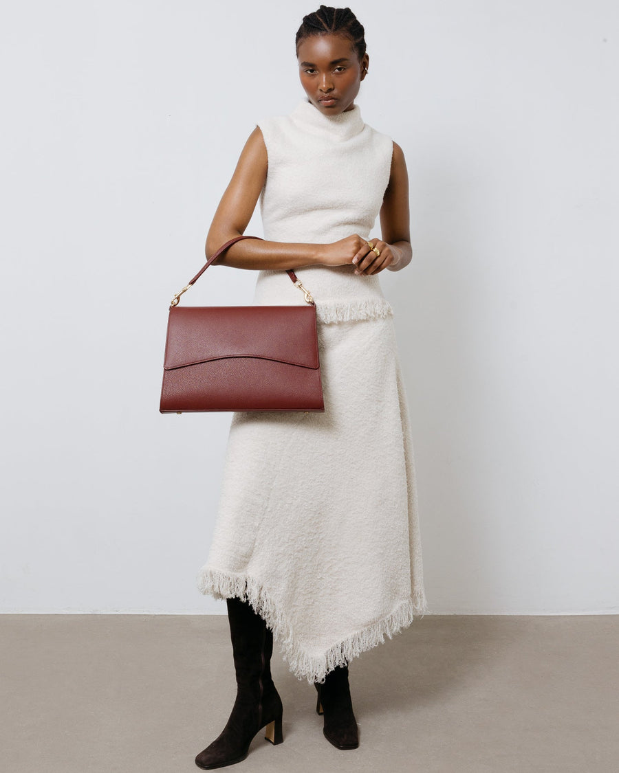 Woman holding a red leather handbag against a plain background