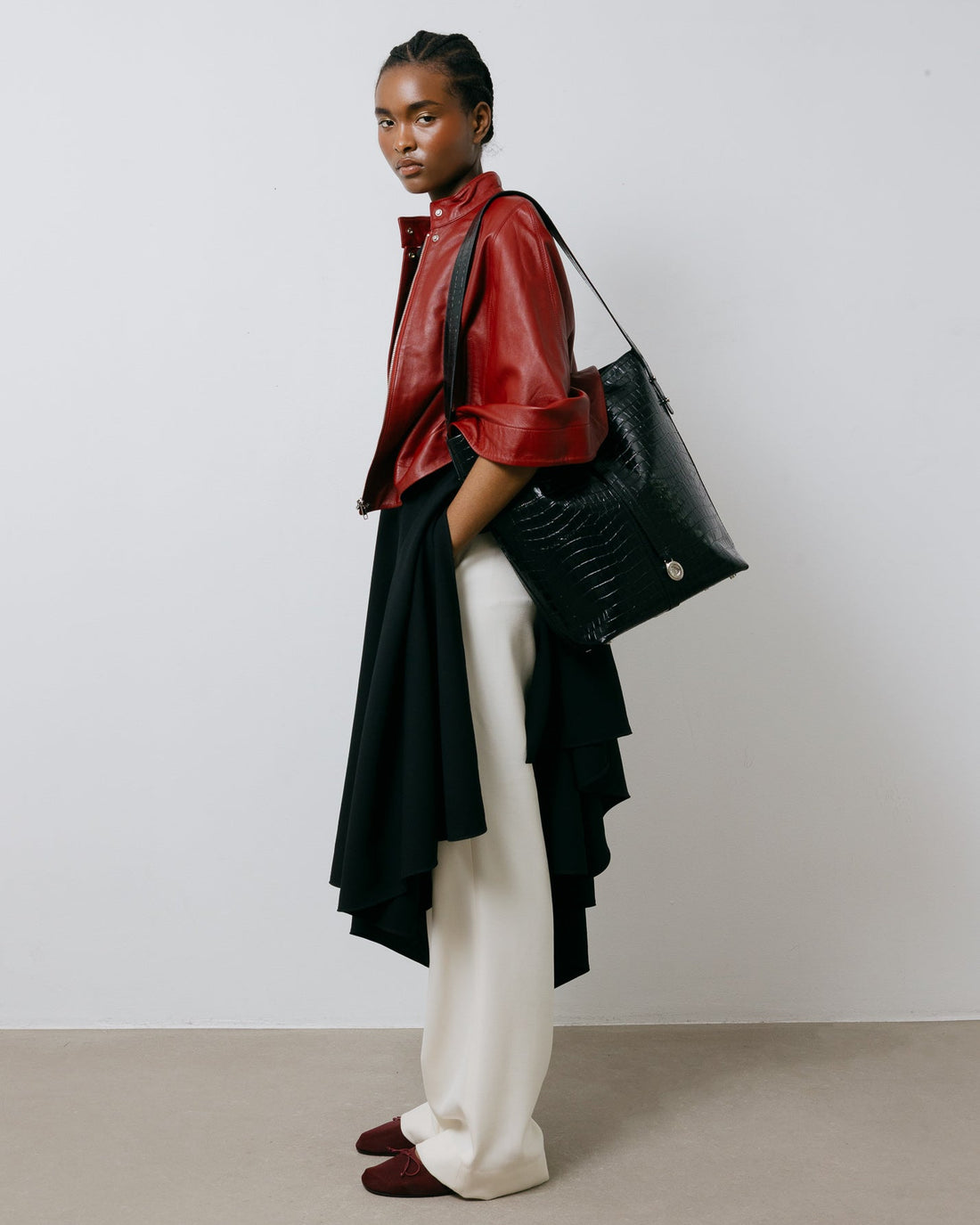 Person wearing a red jacket, black and white outfit, and holding a black bag against a plain background