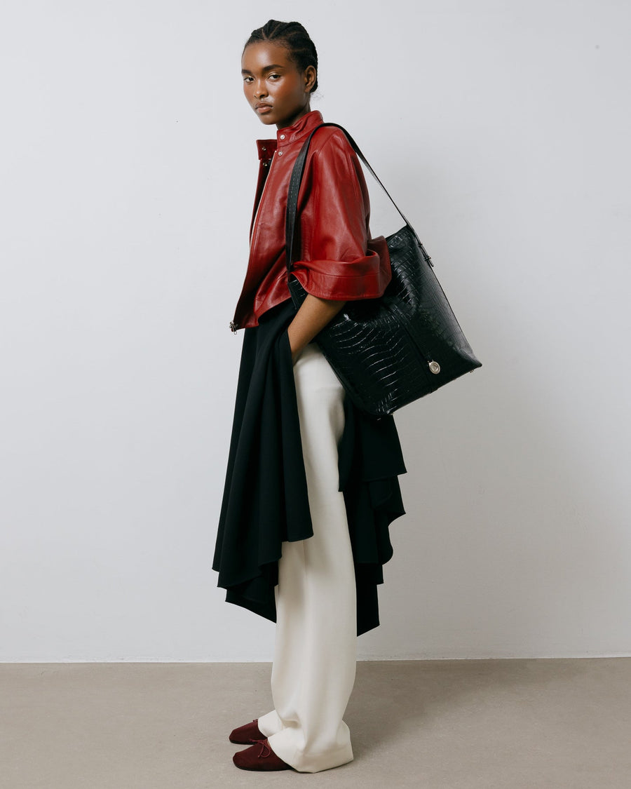 Person wearing a red jacket, black and white outfit, and holding a black bag against a plain background