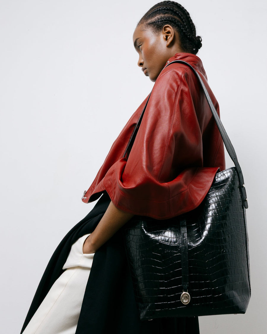 Woman holding a black crocodile-patterned handbag against a plain background