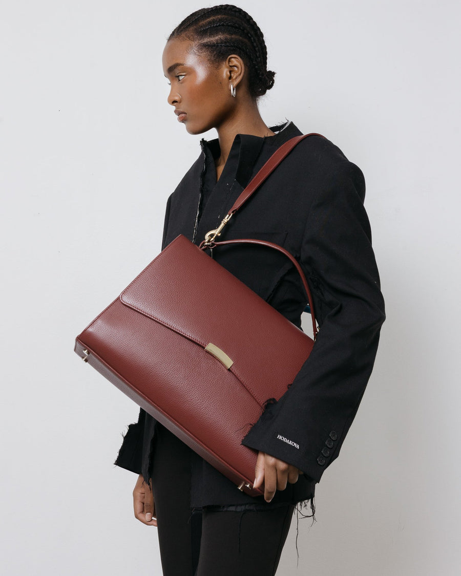 Person holding a maroon leather bag against a plain background